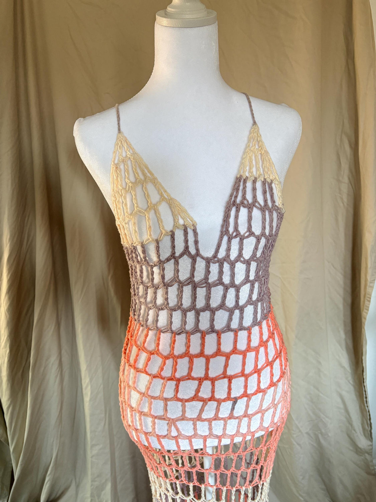 Mannequin wearing a crochet dress with a gradient color pattern against a beige background