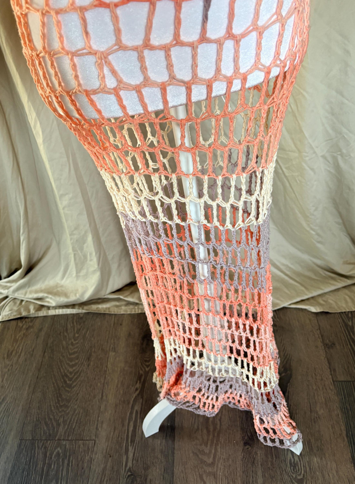 Bottom of a crocheted beach dress with gradient colors on a wooden floor.