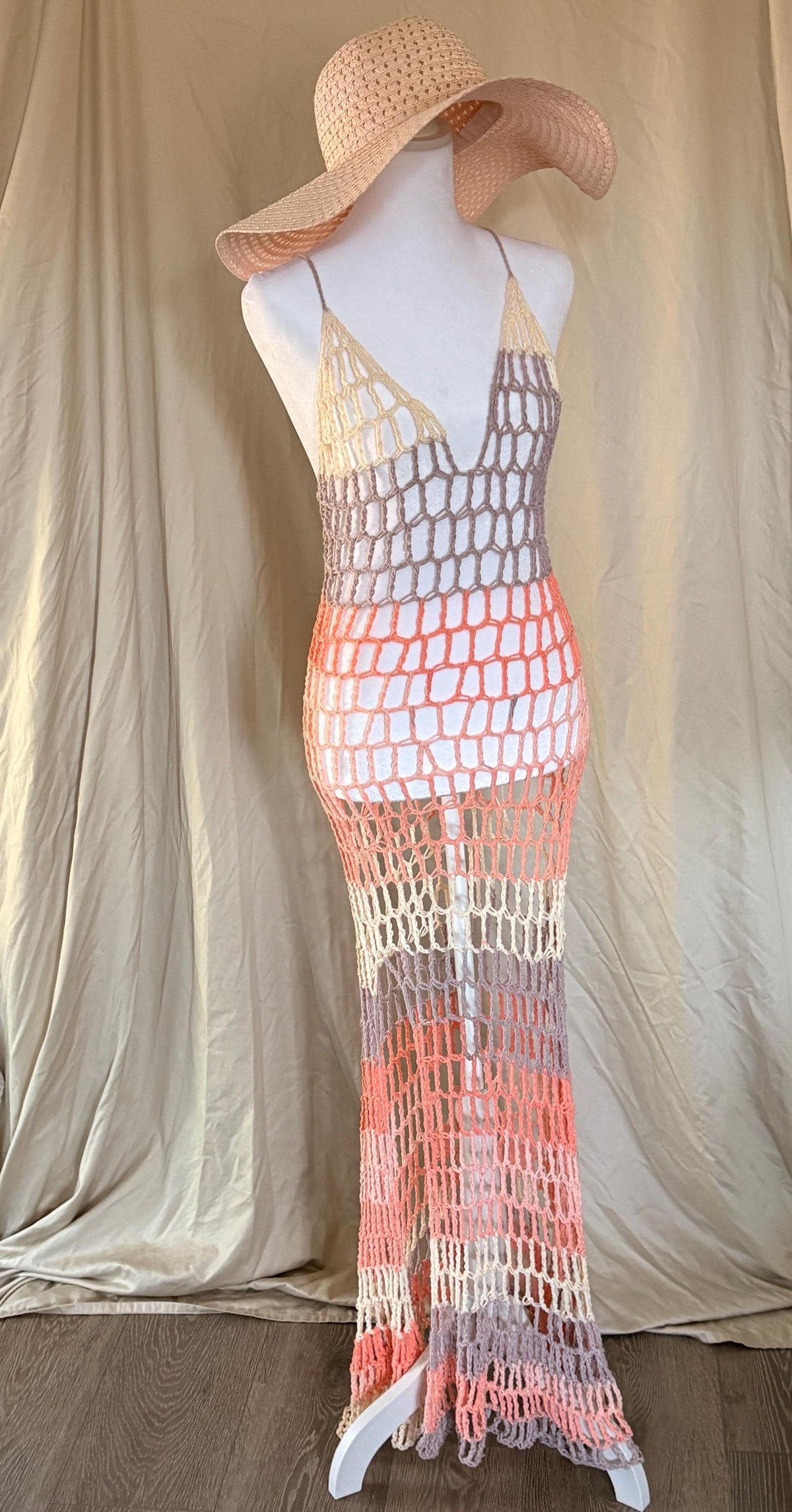 Mannequin wearing a colorful crochet dress with a wide-brimmed hat against a beige background