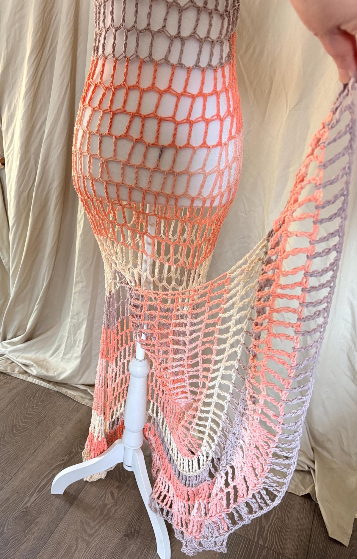 Bottom of a crochet dress with a gradient pattern with a hand holding open the slit to show the bottom of the dress against a neutral background